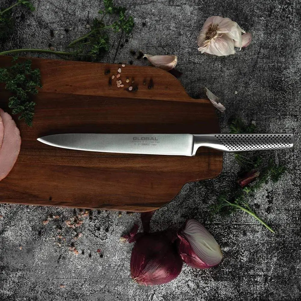 Chef's knife on a wooden cutting board with vegetables on a dark surface