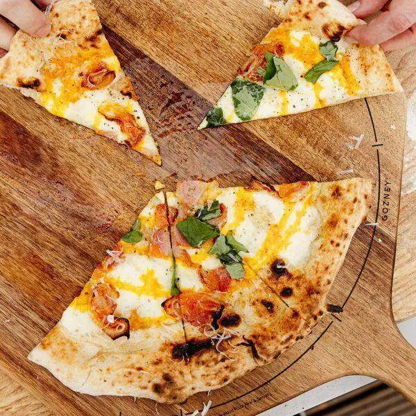 Gozney Acacia wood pizza peel with fresh pizza slices, served on a wooden board, Cookin Stores kitchenware.