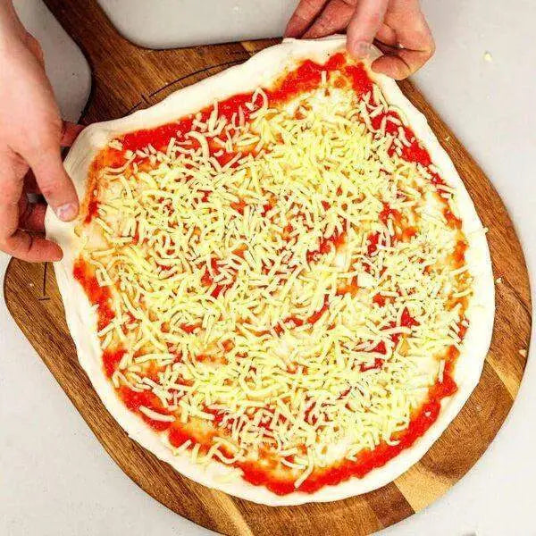 Uncooked pizza with cheese and tomato on acacia wood pizza peel from Cookin Stores