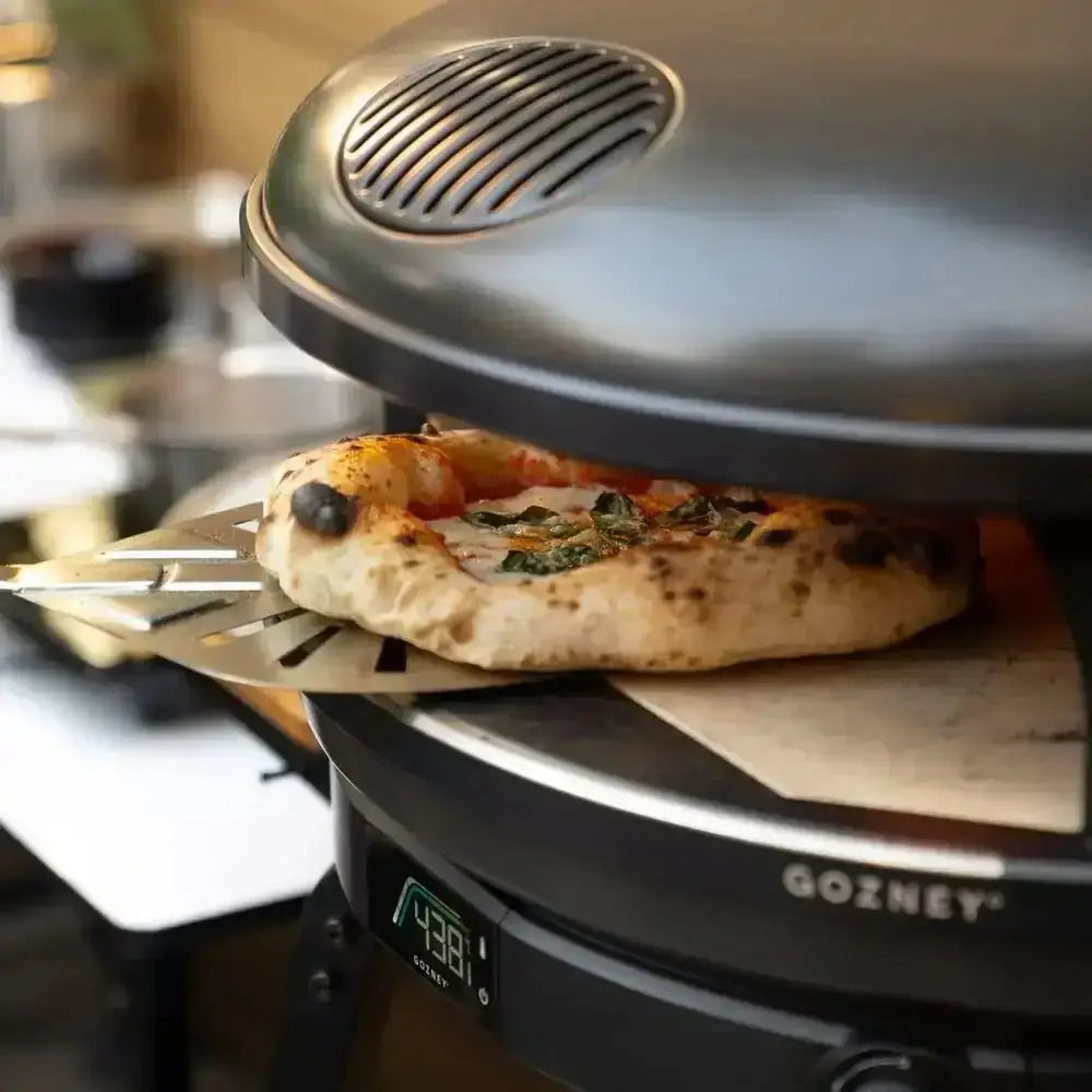 A freshly baked pizza with basil on a metal spatula in a sleek black gozney arc 14 compact outdoor pizza oven