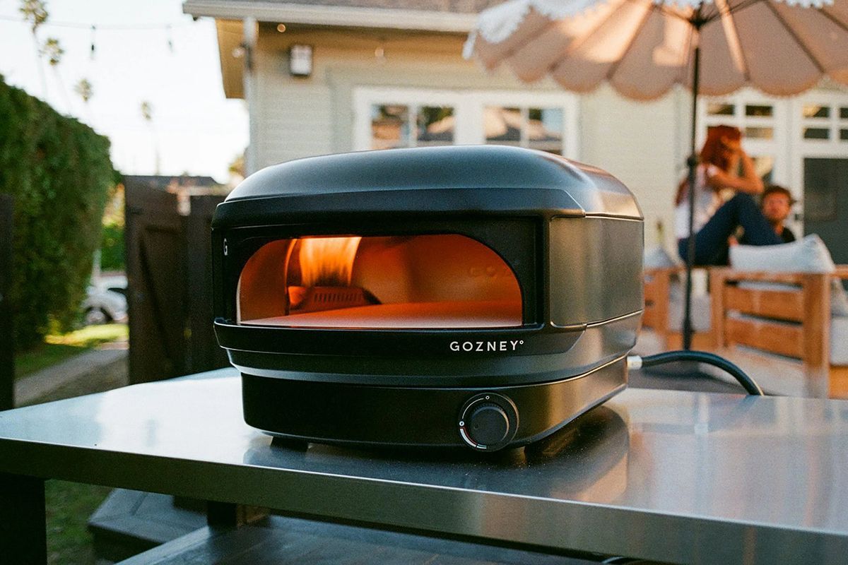 Black Gozney pizza oven on a table outdoors with people in the background.