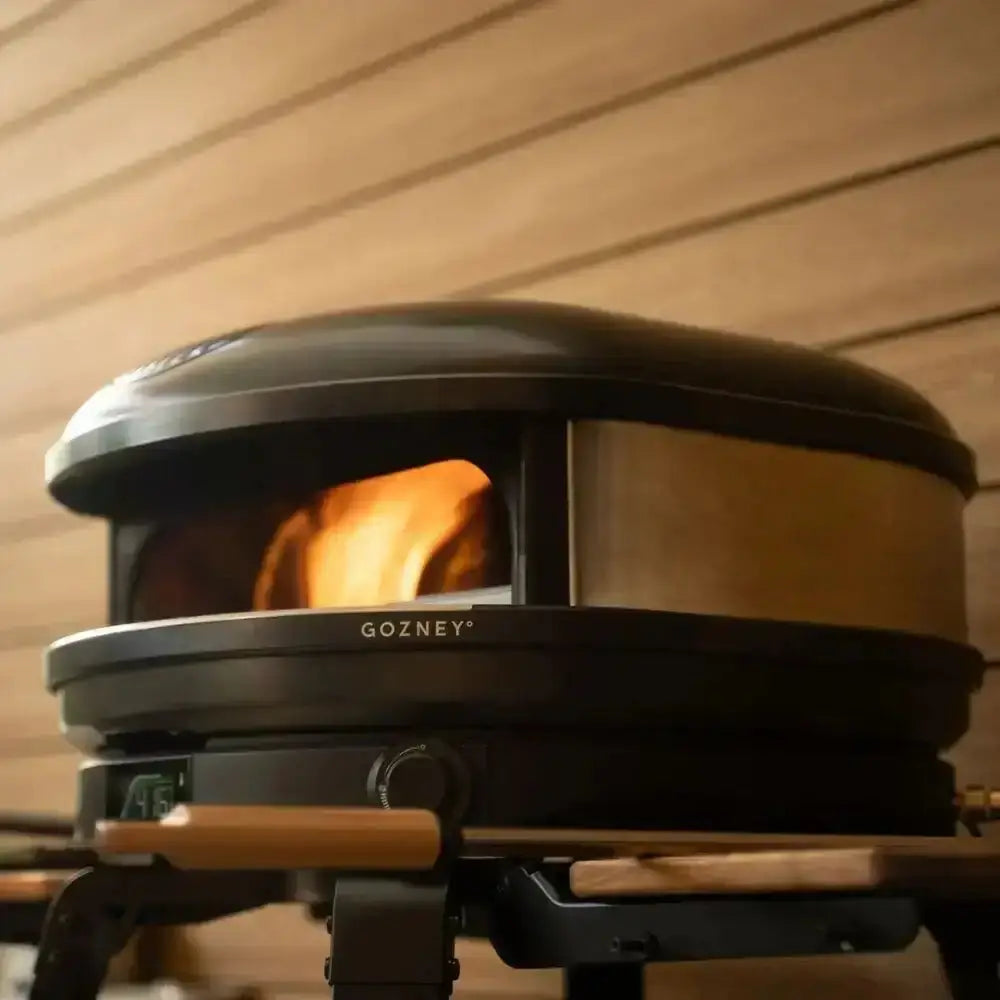 Gozney Arc XL 16 compact outdoor pizza oven in black with wood-fired flame, on patio at Cookin Stores
