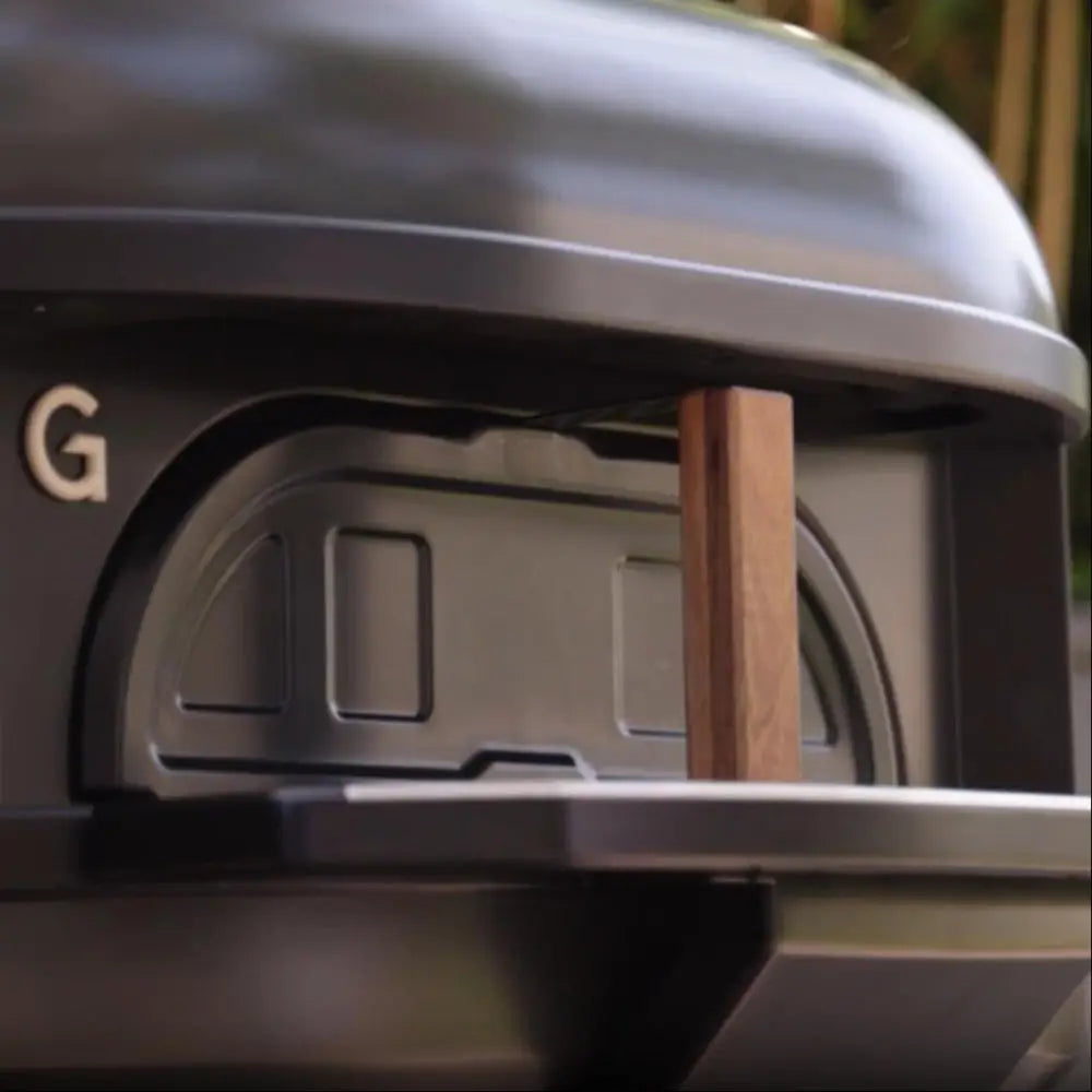 Close-up of outdoor pizza oven with a wooden stick inserted.