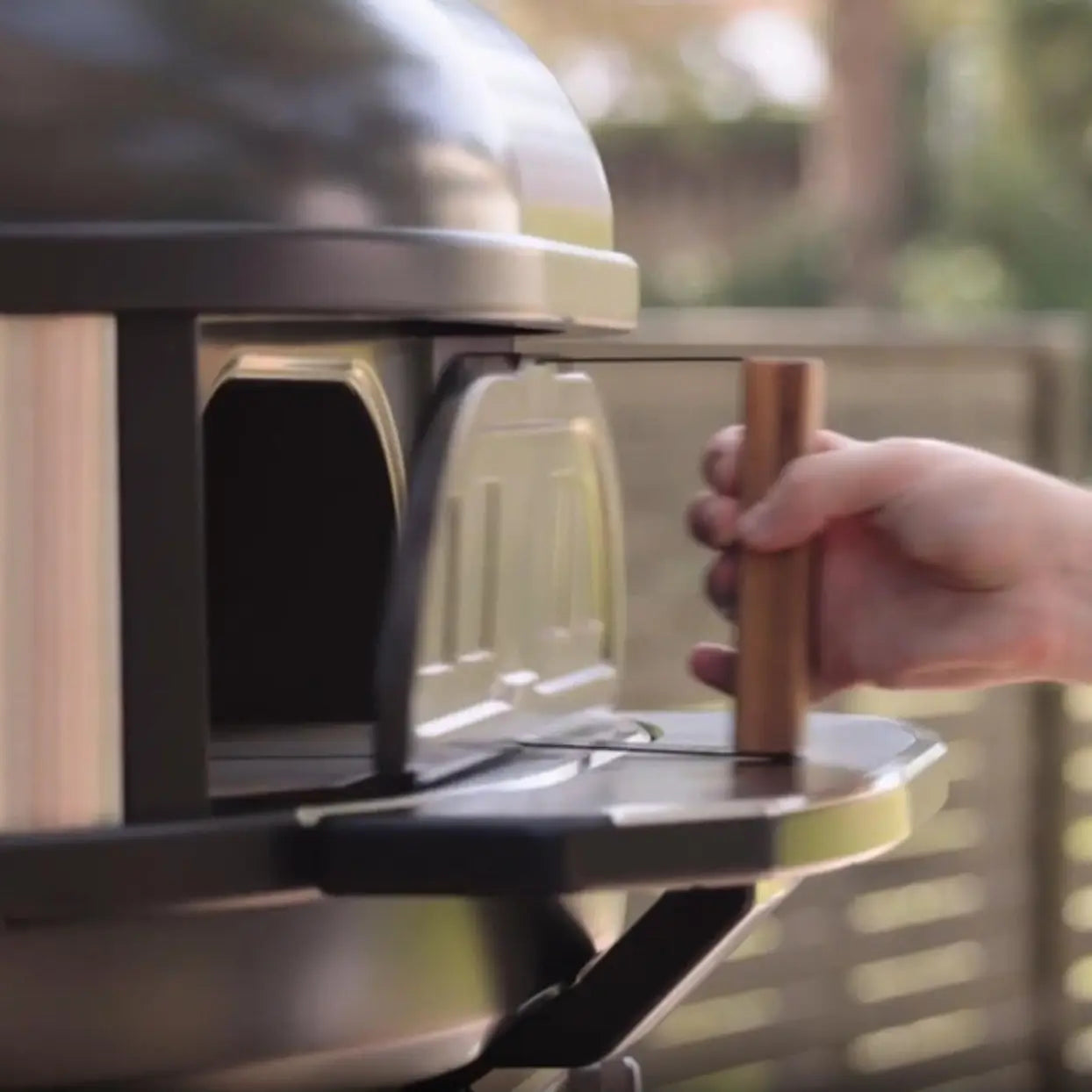 Person opening a silver pizza oven with a wooden handle