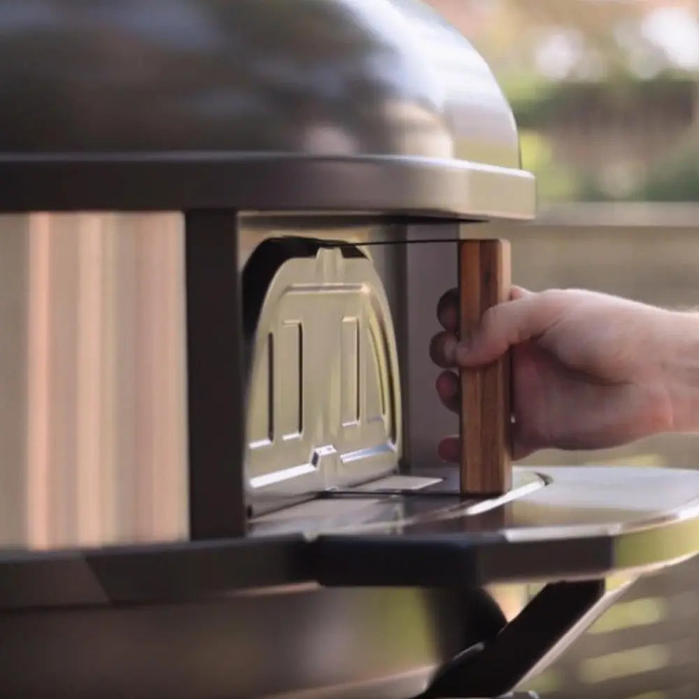 Person opening a stainless steel grill lid with a wooden handle.