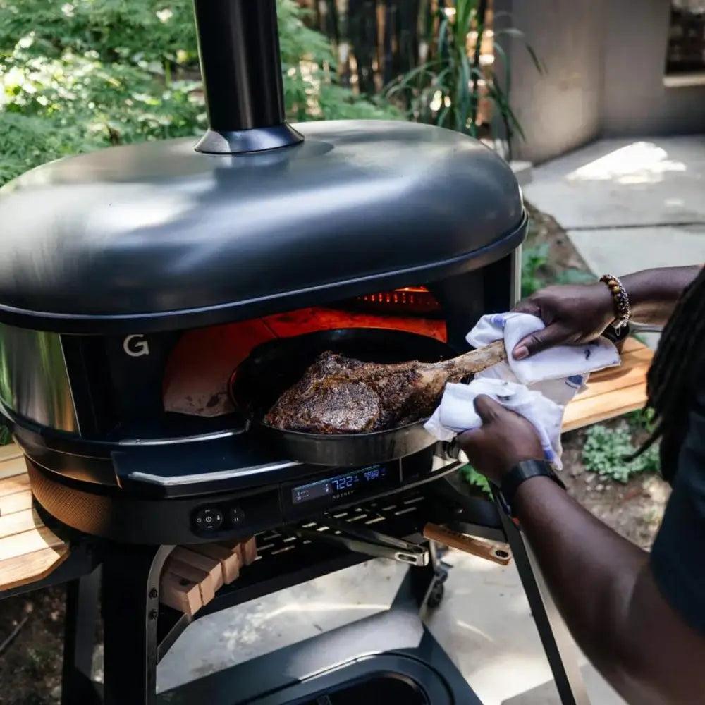 Person cooking on a portable pizza oven in an outdoor setting