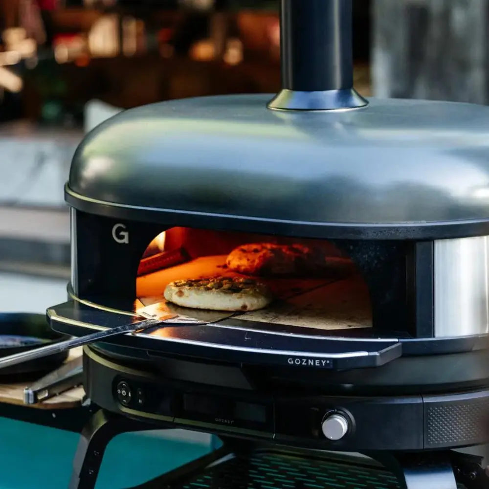 Portable pizza oven with pizzas inside, brand 'Gozney' visible