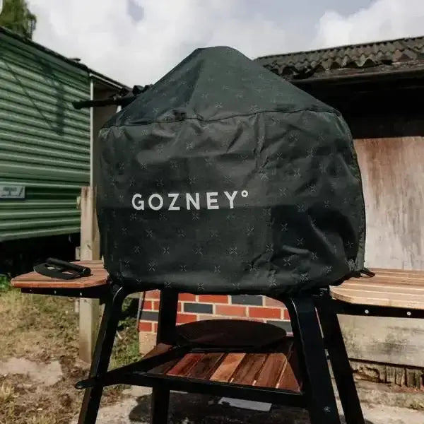 Gozney Dome outdoor pizza oven with black cover on wooden stand in backyard setting