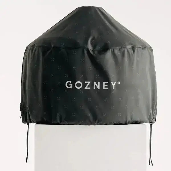 Gozney Dome outdoor pizza oven cover in black with logo, shown on a white stand