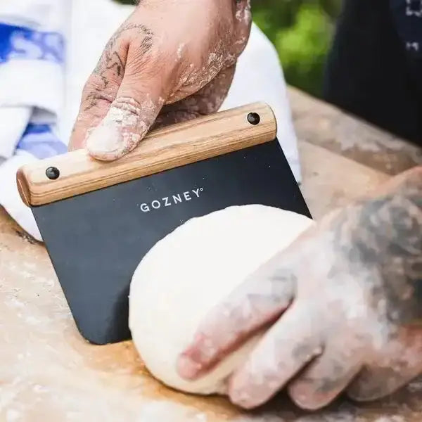 Gozney pizza dough cutter with wooden handle in use on fresh dough, kitchenware at Cookin Stores