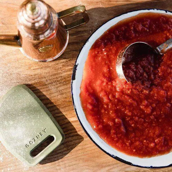 Gozney pizza dough scraper, sauce dish with ladle, and oil can on wooden countertop at Cookin Stores