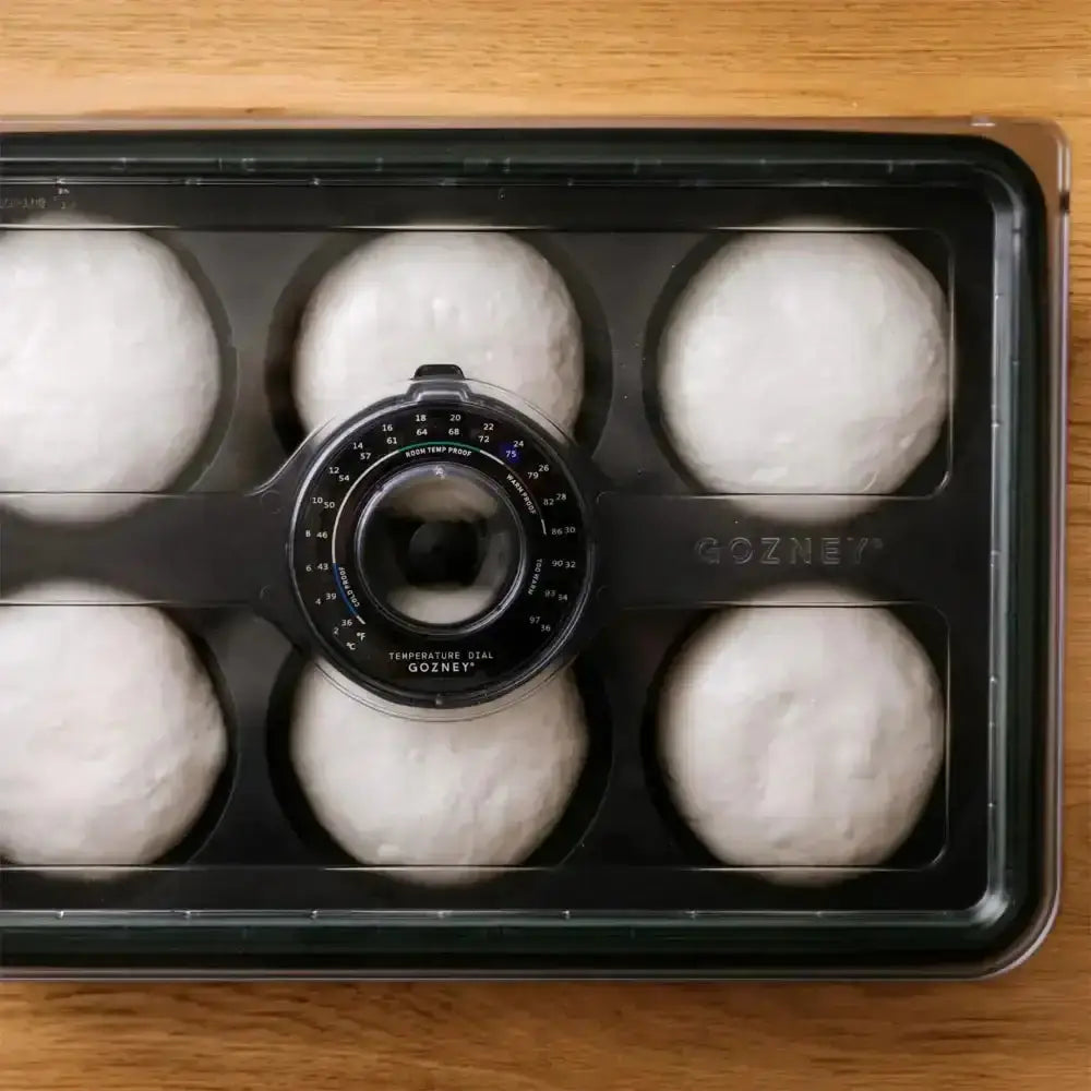 Bread dough in a black container with a Gozney branding on a wooden surface
