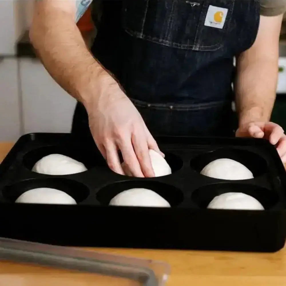 Person placing dough balls into a black baking tray on a wooden surface.