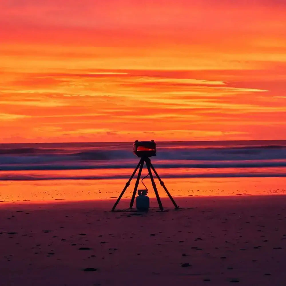 Gozney Tread portable outdoor pizza oven set up on a beach at sunset, vibrant orange sky