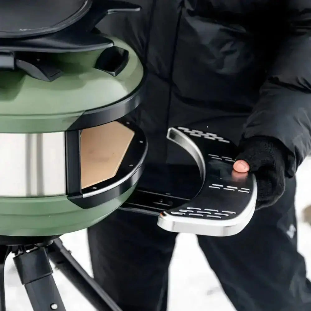 Person attaching Gozney Tread Mantel to green outdoor pizza oven in winter setting