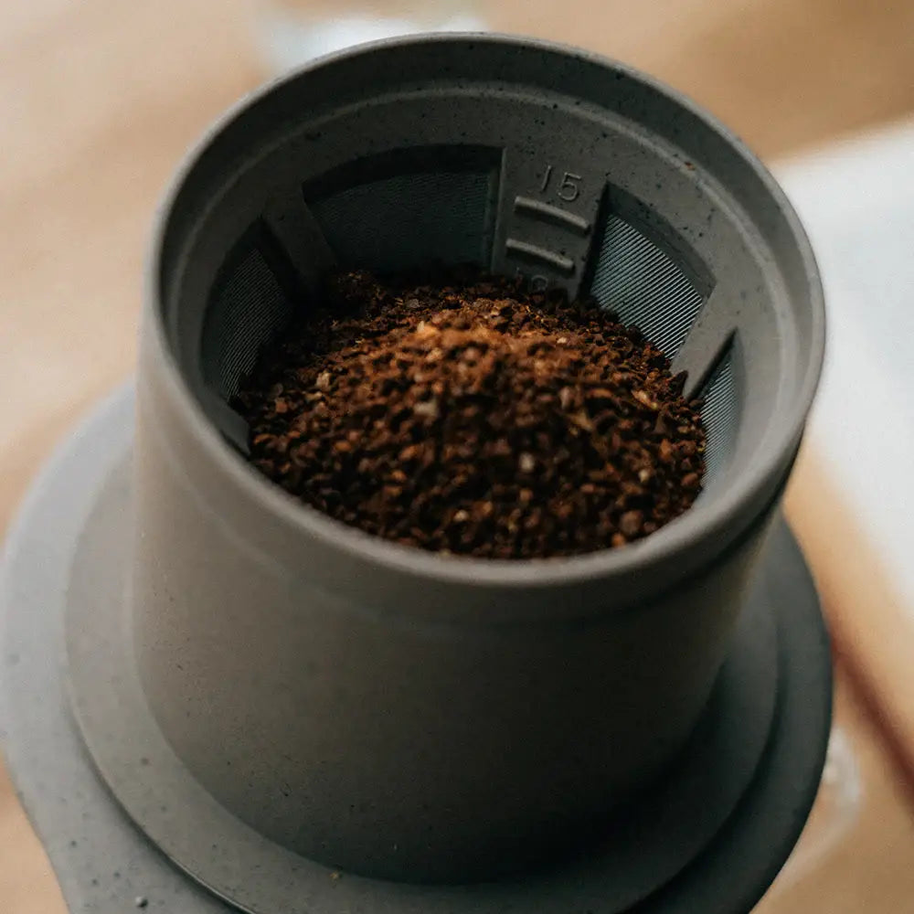 Gray ceramic hario baton cafeor paperless coffee dripper filled with dark brown ground coffee for brewing