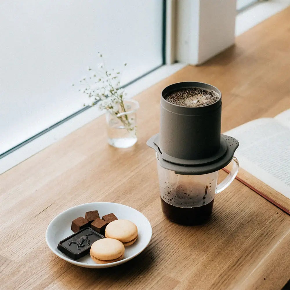 Gray hario baton cafeor paperless coffee dripper with clear glass carafe and dark brown grounds inside top chamber