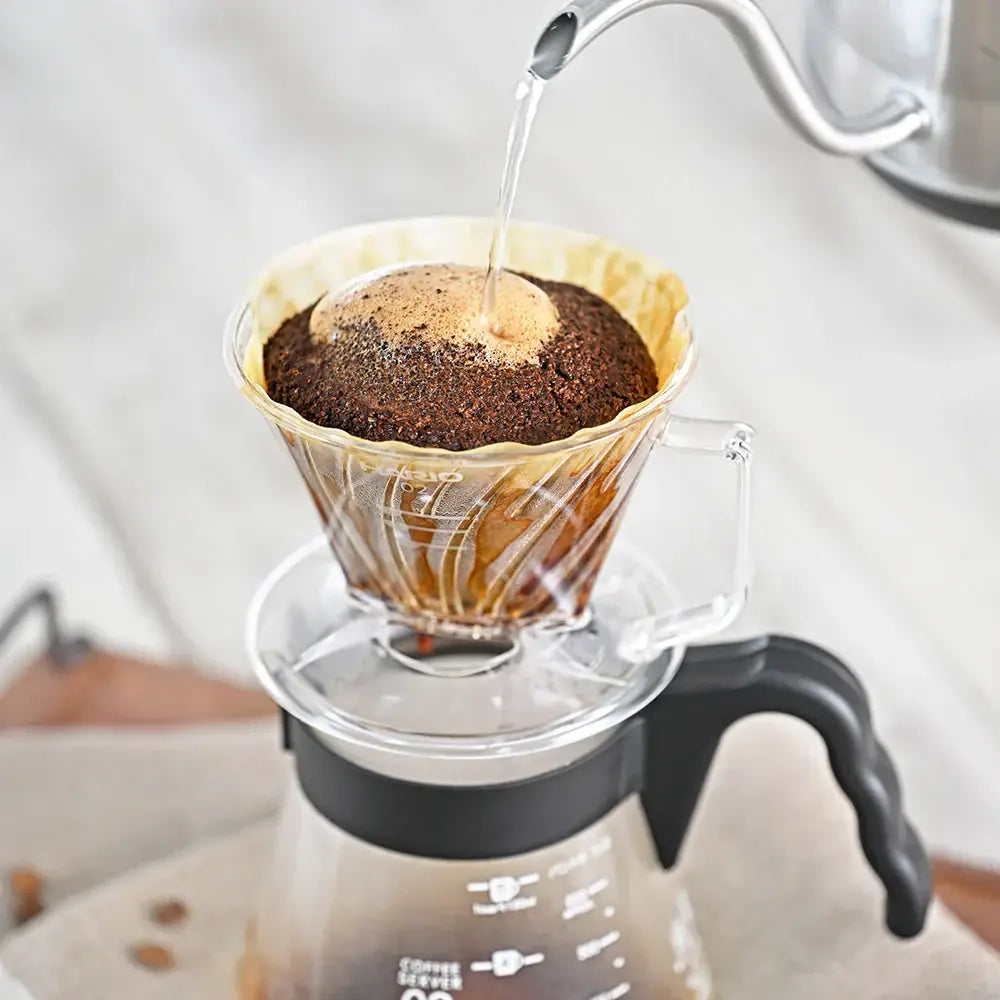 Coffee being poured into a glass coffee maker with a filter.
