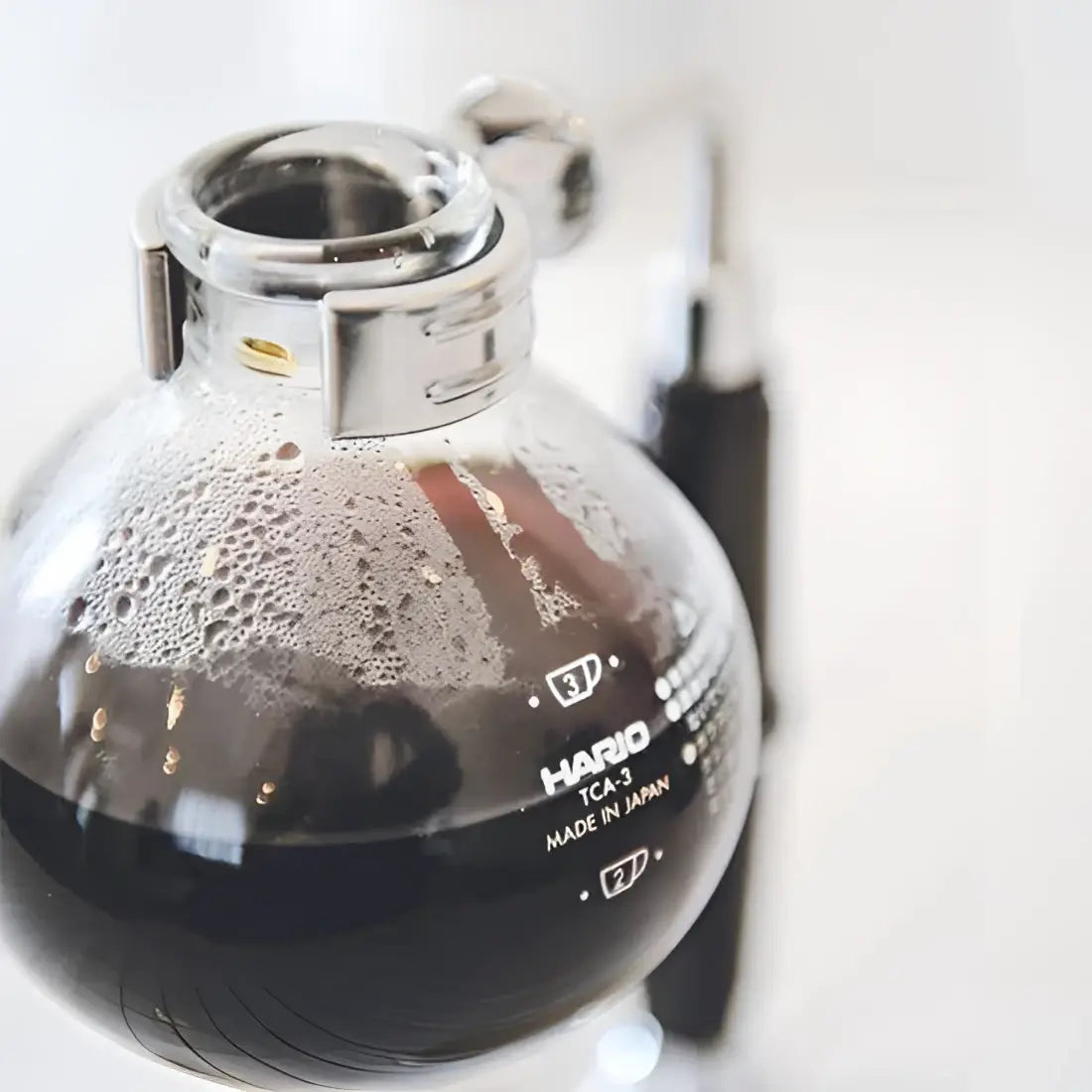 Clear glass coffee brewer with silver lid on a white background