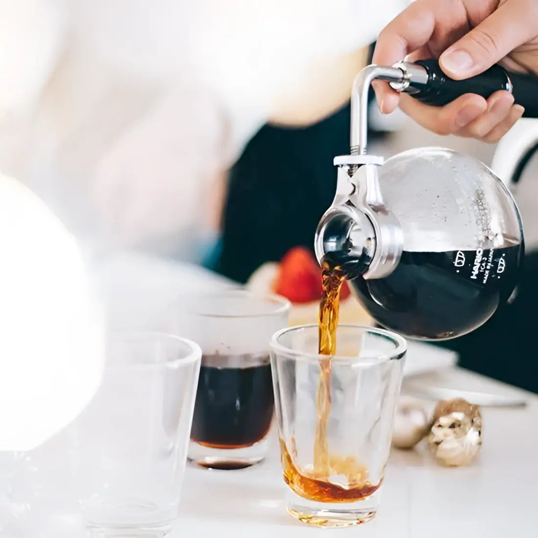 Person pouring coffee from a siphon into a glass on a blurred background