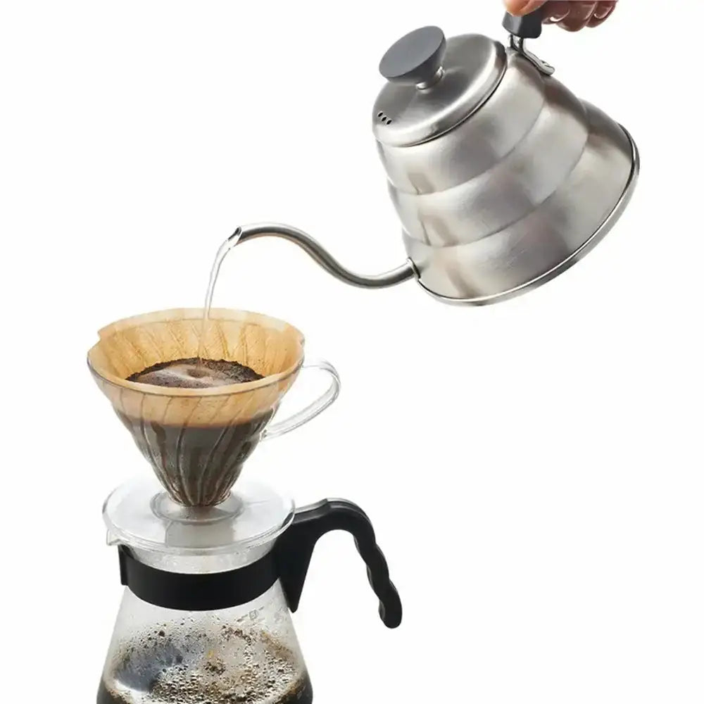 Stainless steel kettle pouring water into a wooden coffee filter over a glass carafe.