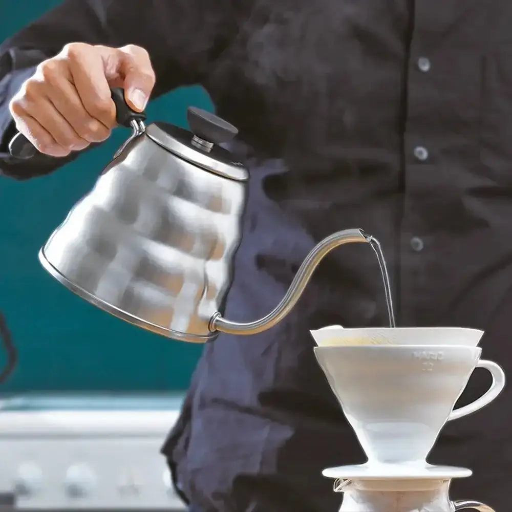 Person pouring coffee from a stainless steel kettle into a white coffee filter.