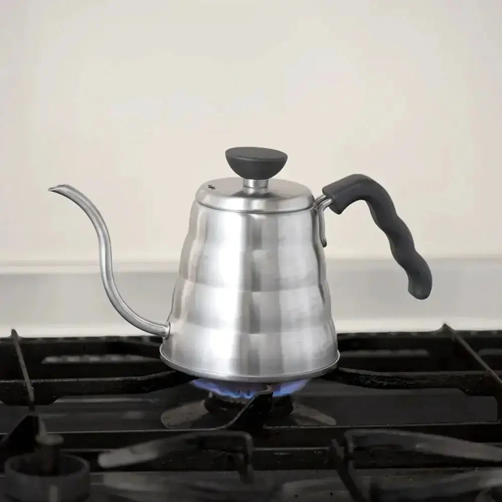 Stainless steel gooseneck kettle on a gas stove with a white background