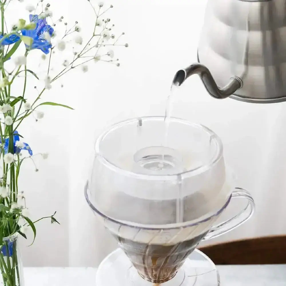 Pouring water from a kettle into a glass coffee filter with coffee beans.