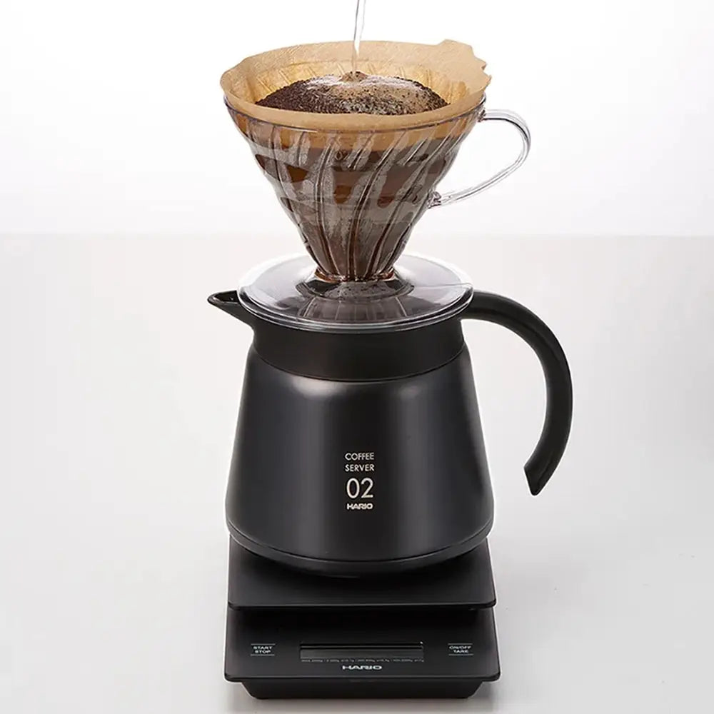 Black coffee server with a paper filter and coffee grounds on a white background