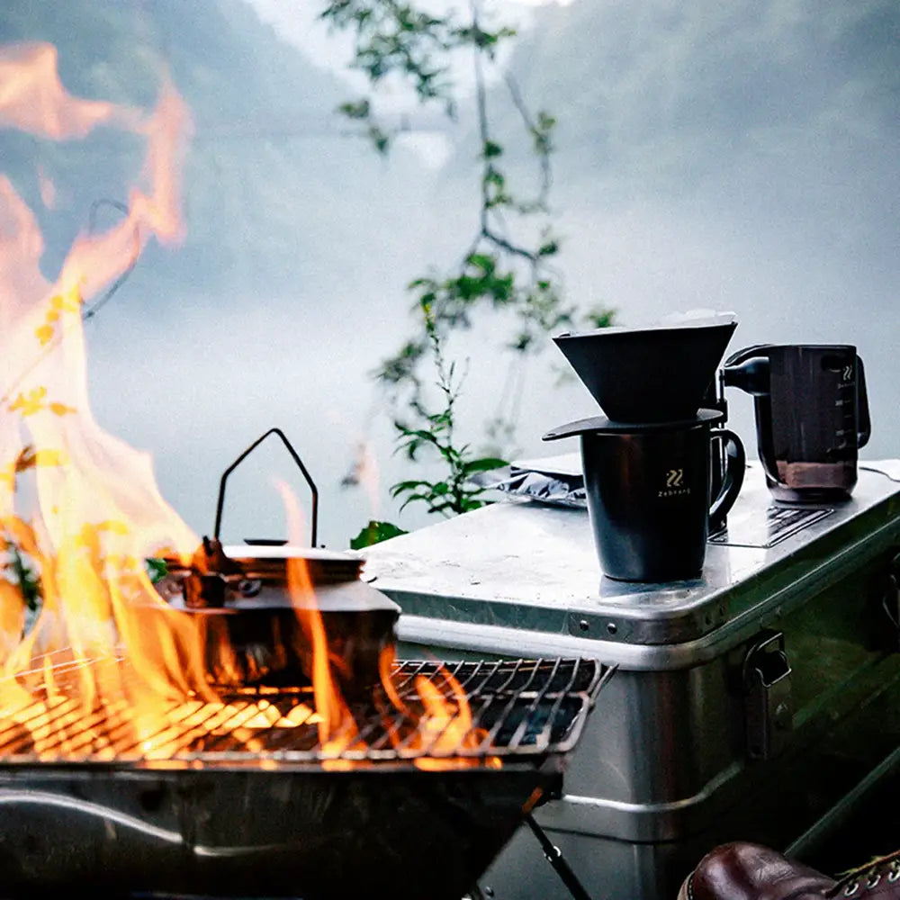 Camping stove with coffee maker and mugs near a campfire outdoors