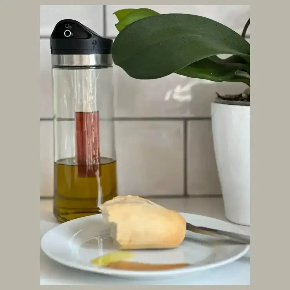 Glass oil dispenser with olive oil on a plate with bread, against a kitchen backdrop.