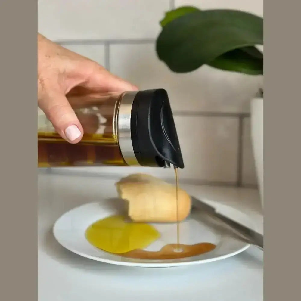 Hand pouring honey from a bottle onto a plate with bread.