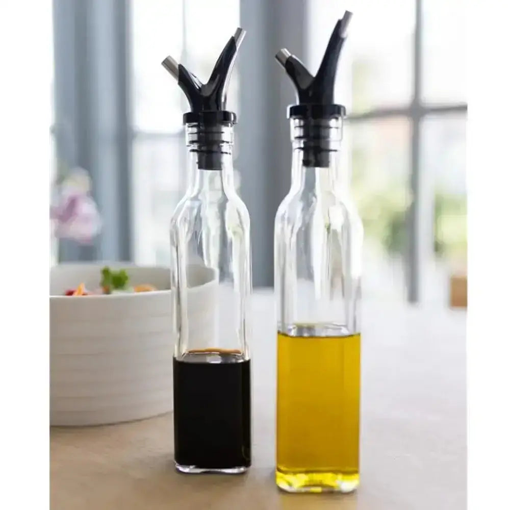 Two glass bottles with black nozzles containing oil and vinegar on a blurred kitchen background.