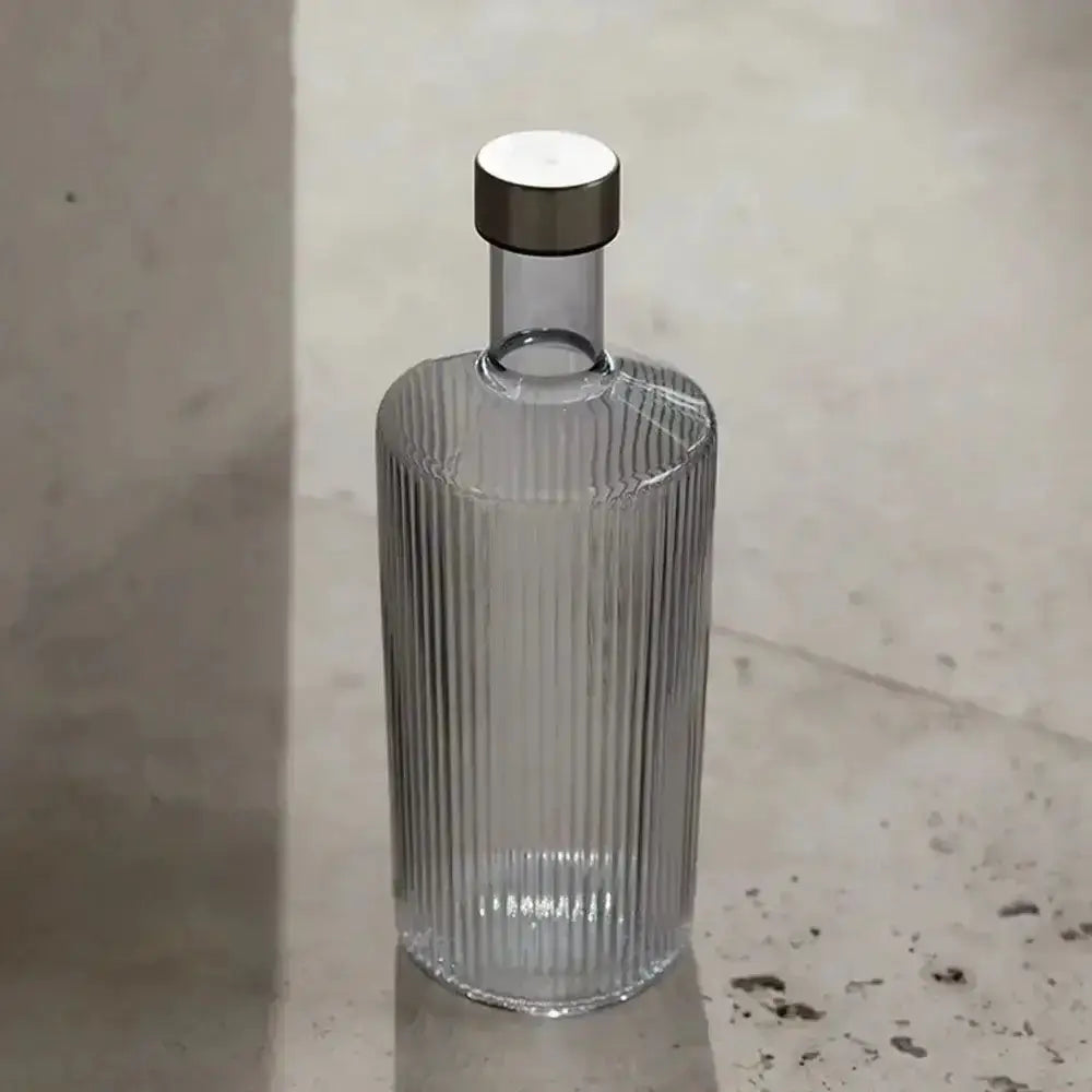 Clear glass bottle with ribbed design and black cap on a textured surface