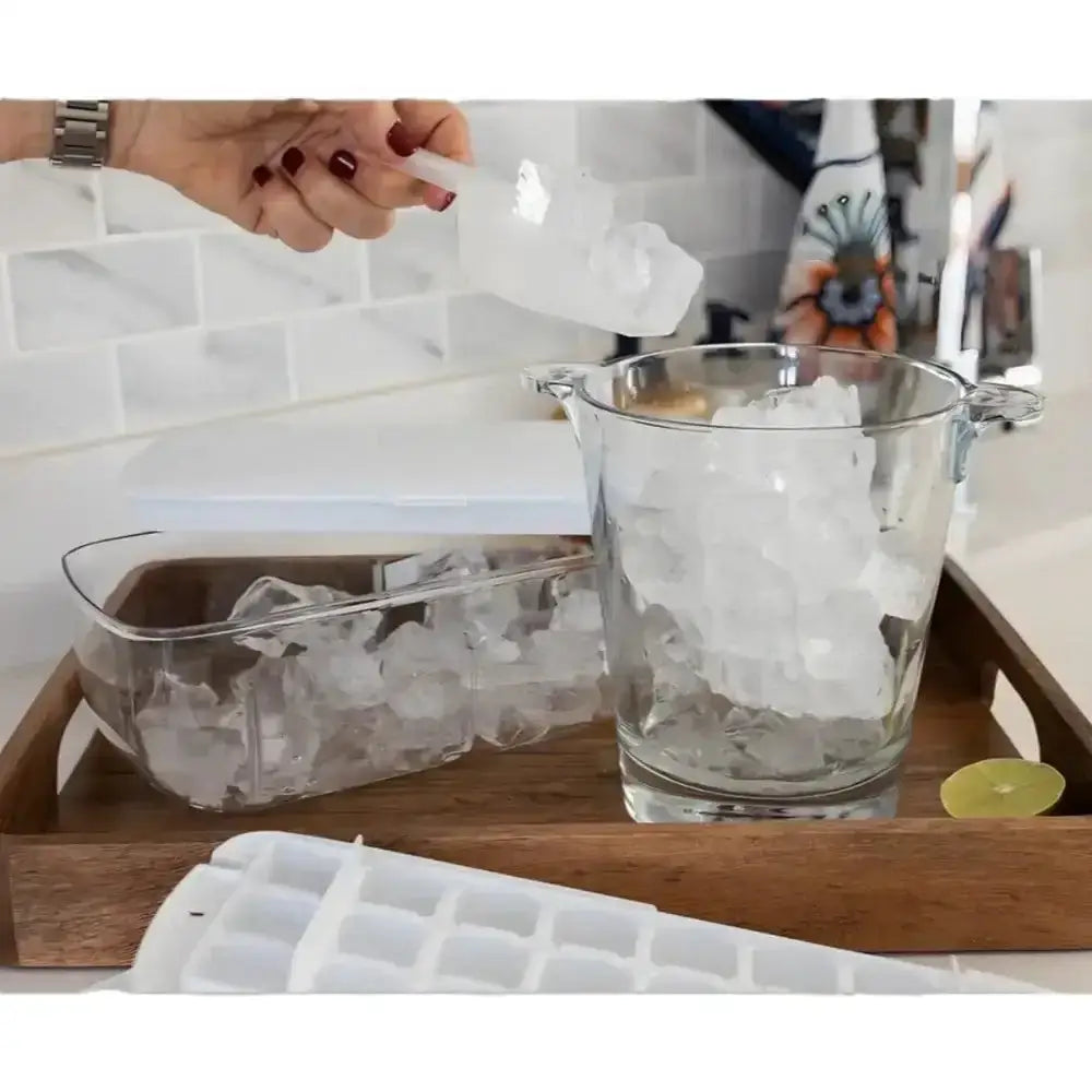 Person pouring water into a glass filled with ice cubes on a wooden tray.
