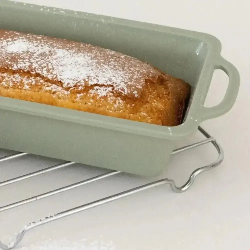 Non-stick silicone loaf pan with baked cake, sprinkled with powdered sugar, on cooling rack