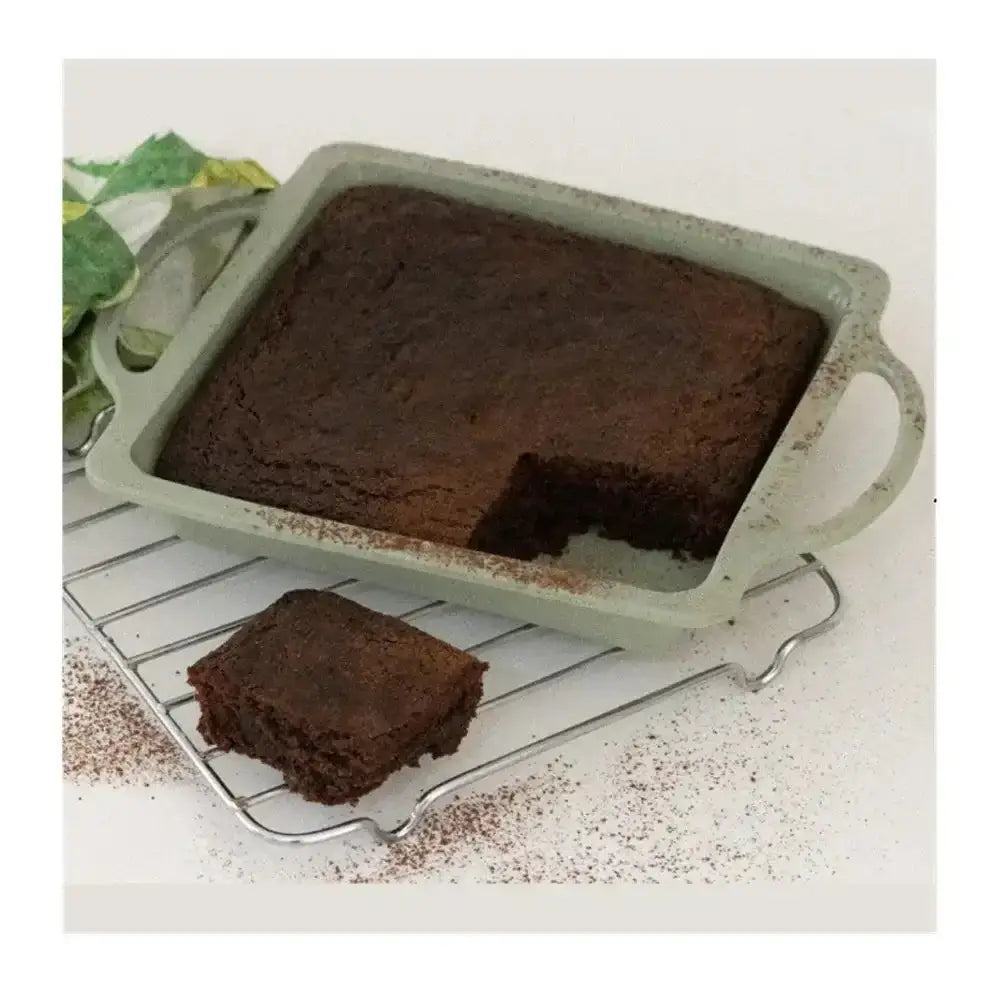 Chocolate cake in a green baking dish with a piece removed on a cooling rack.