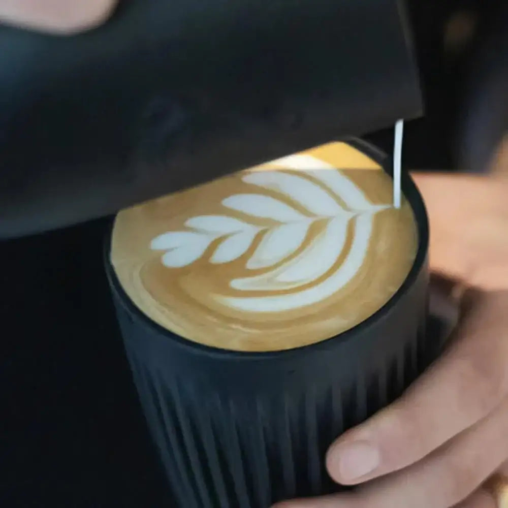 Person making a latte art design on a coffee cup with a black sleeve.