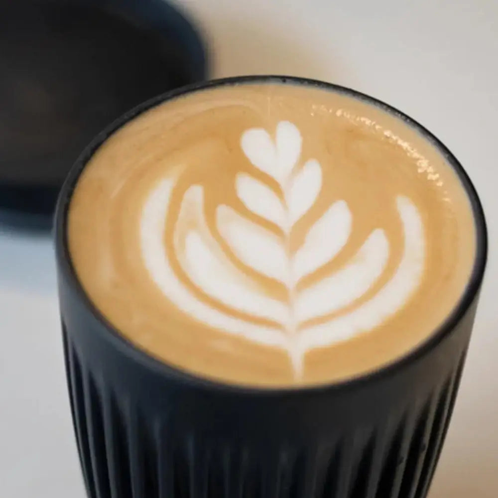 Cappuccino with latte art in a black cup on a blurred background