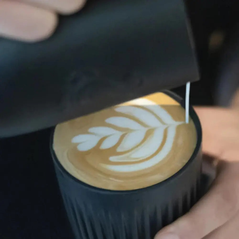 Person pouring a dark liquid into a cup with latte art, likely coffee.