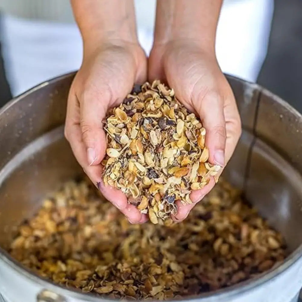 Person holding a handful of coffee husks over a metal bowl filled with more granola.