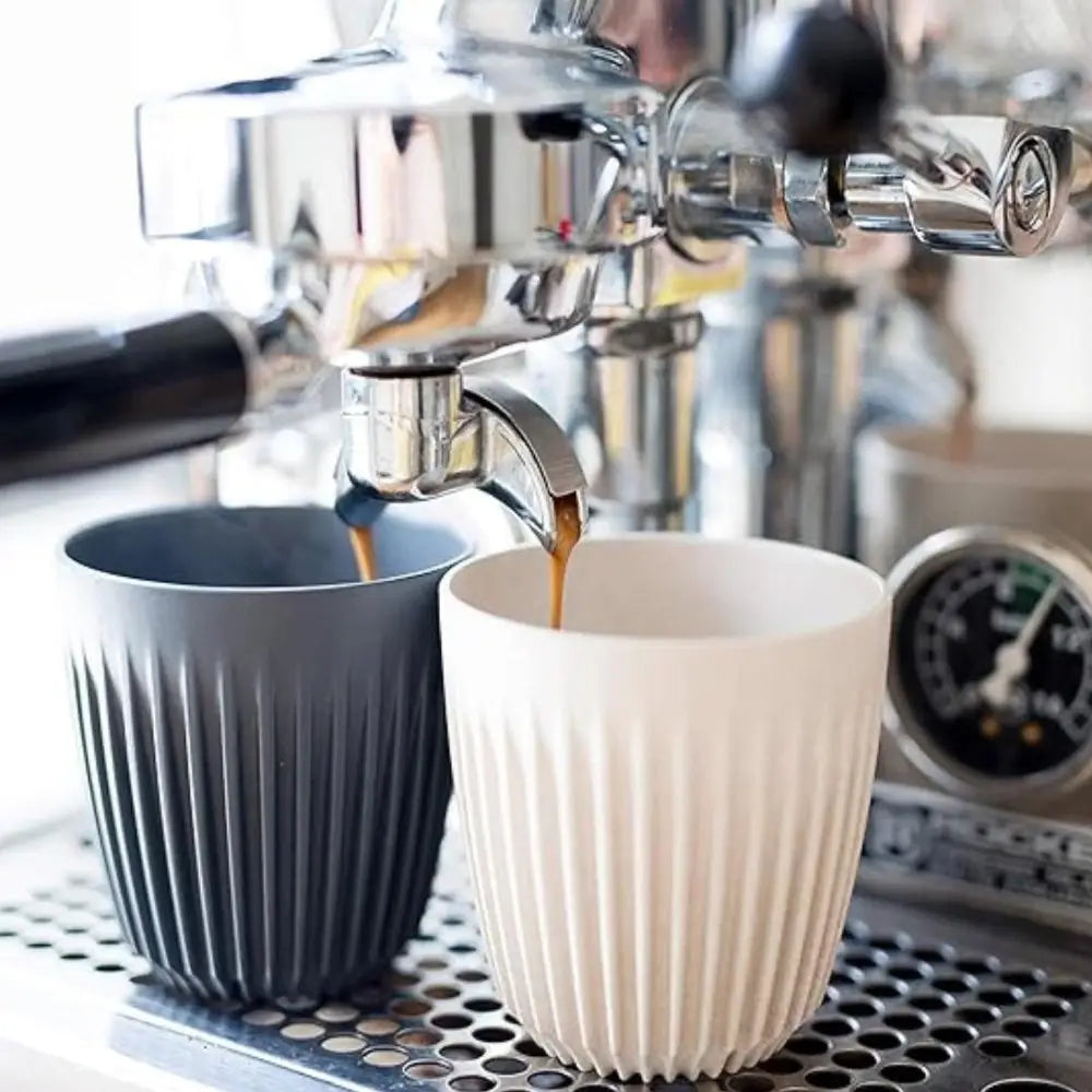 Espresso being poured into two fluted ceramic cups on an espresso machine.