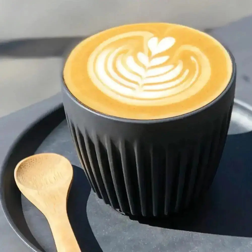 Black textured cup with a latte art design on a dark surface with a wooden spoon.