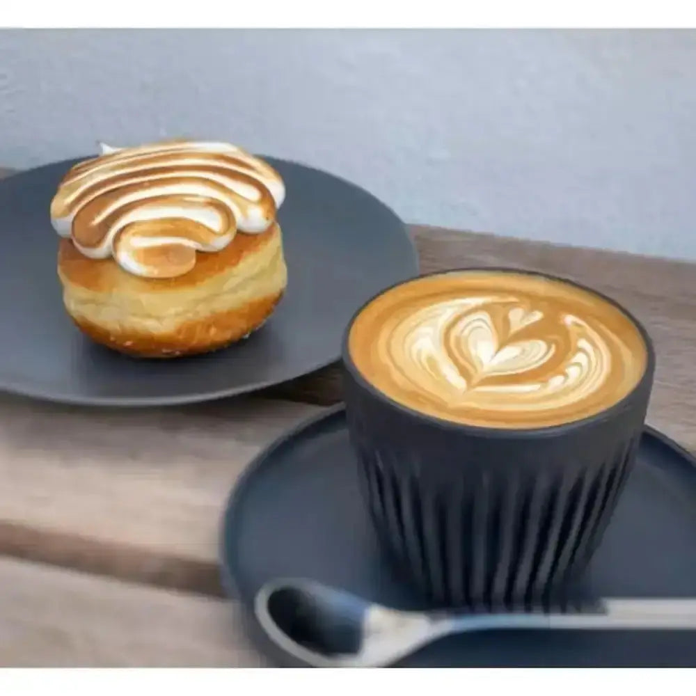 Cappuccino in a black cup with latte art on a wooden table, accompanied by a pastry.