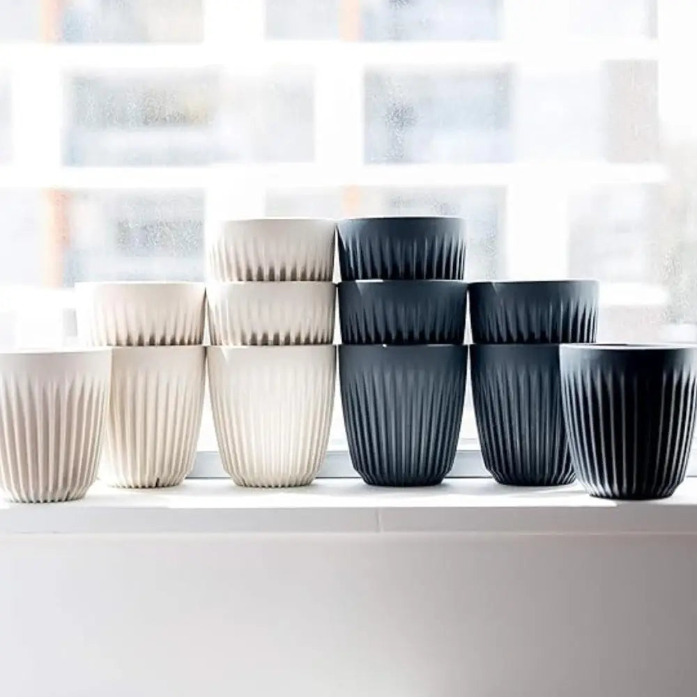 Set of white and black fluted cups on a white surface with a blurred window background