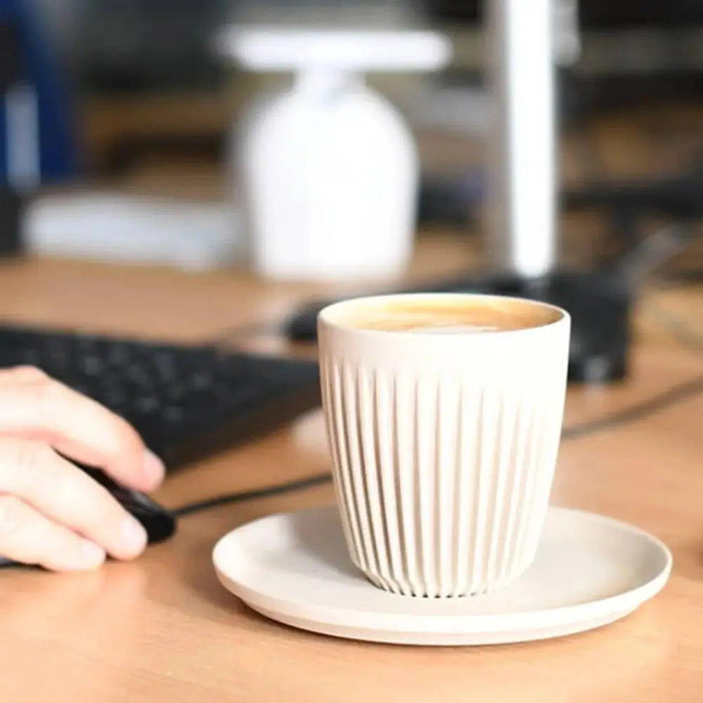 White ceramic cup on a saucer with a blurred office background