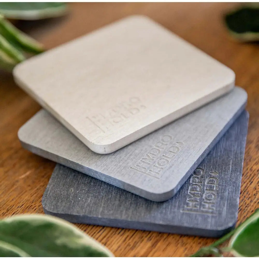 Three square coasters with 'Hydro Hold' branding on a wooden surface.