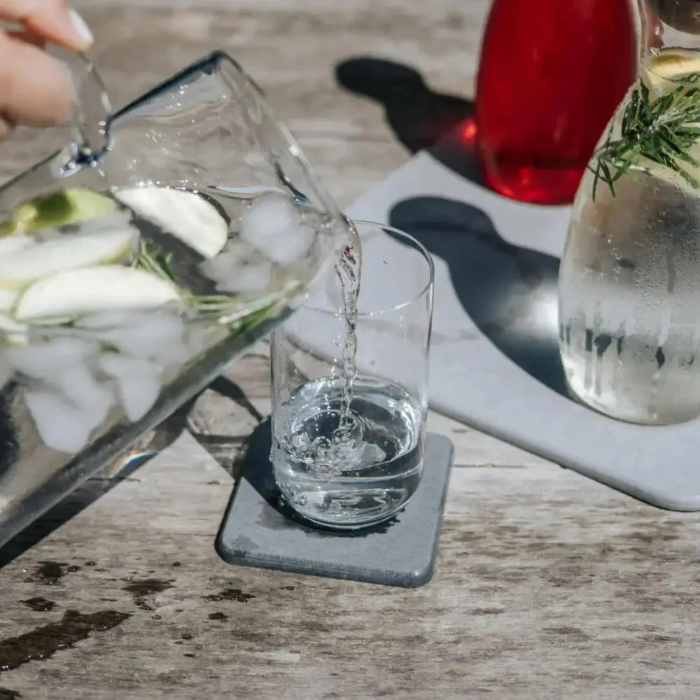 Glass pitcher being filled with iced water on a wooden table.