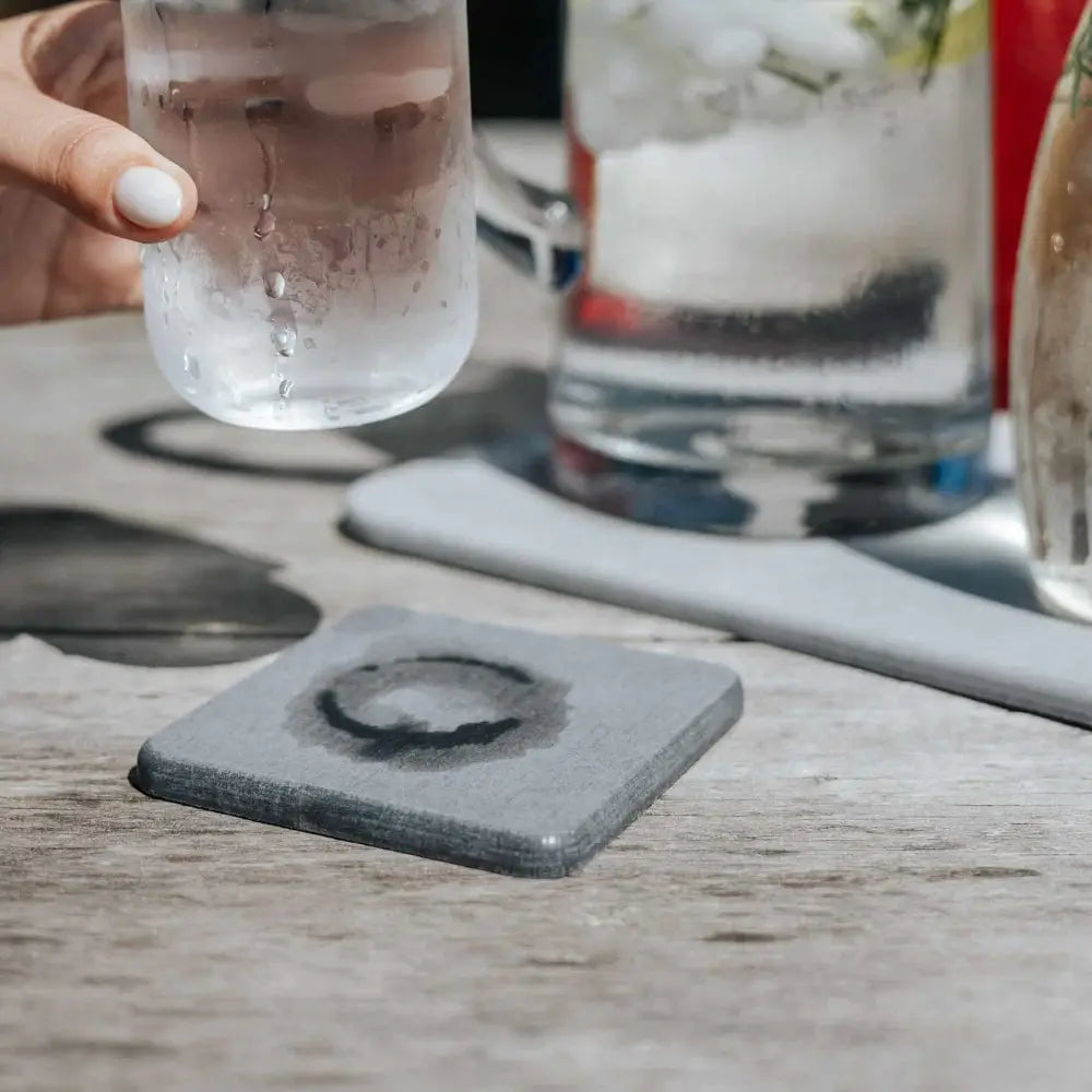 Gray stone coaster with a circular design on a wooden table with glasses of water in the background.