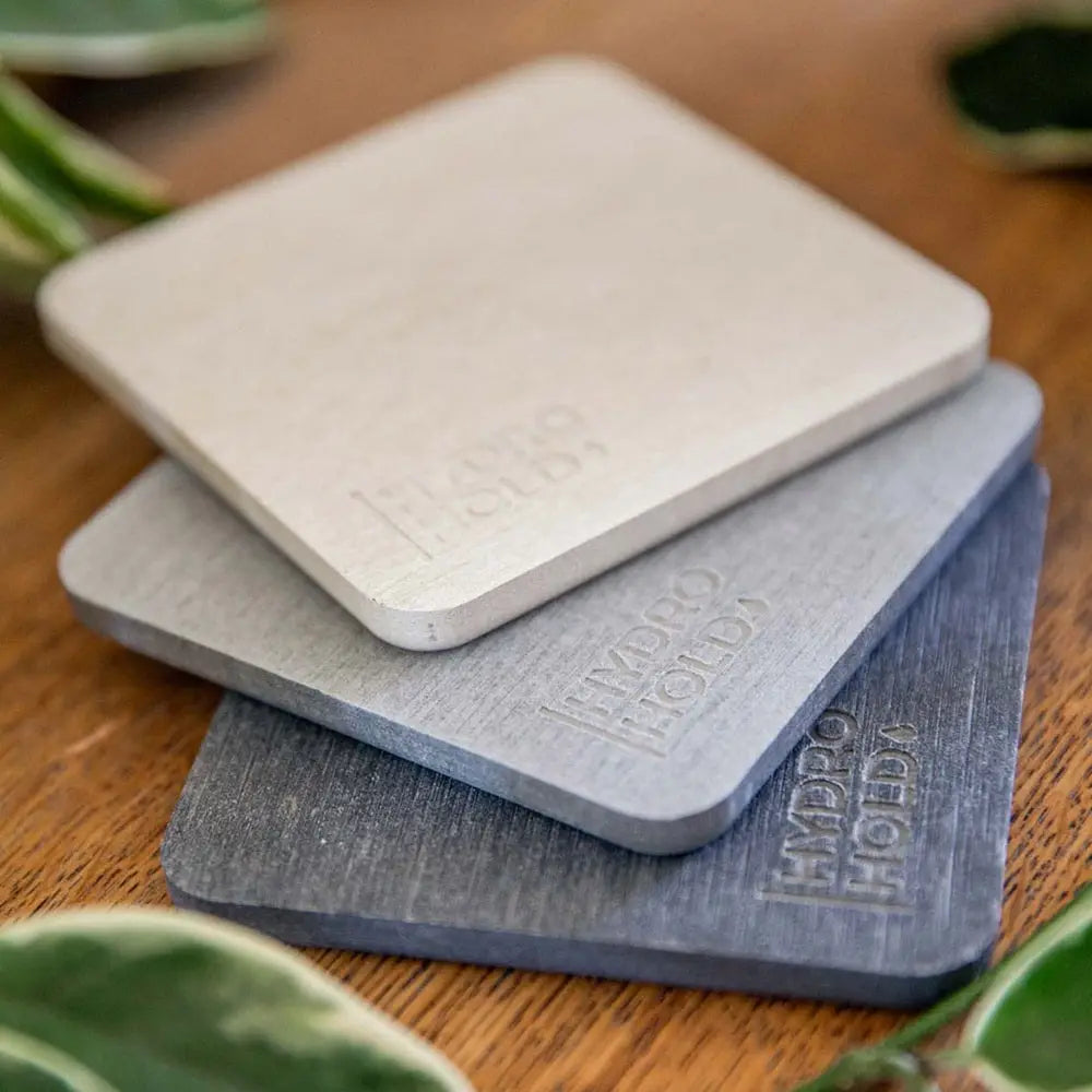 Three square coasters with 'Hydro Hold' branding on a wooden surface.